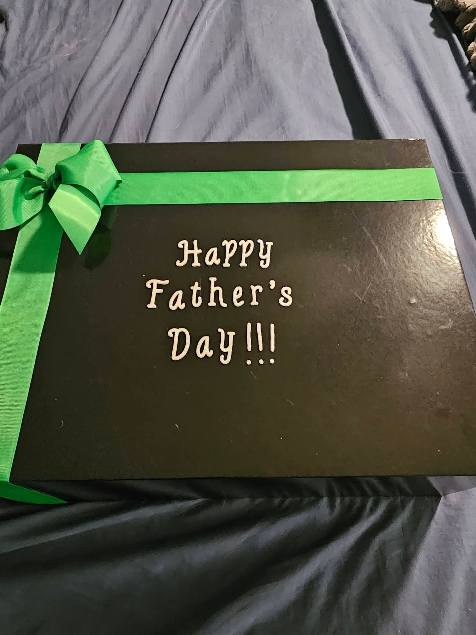 Closed black gift box with a green ribbon bow and Happy Fathers Day lettering